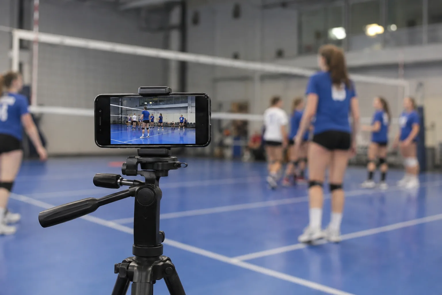A phone on a courtside tripod recording junior volleyball practice